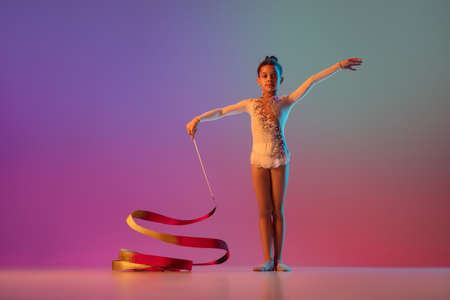 African-american rhythmic gymnast, pretty girl practicing on gradient studio background in neon lightの写真素材
