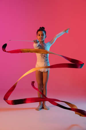 African-american rhythmic gymnast, pretty girl practicing on gradient studio background in neon lightの写真素材