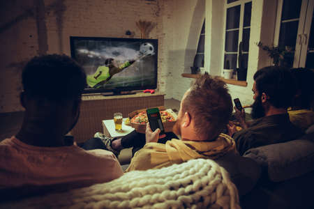 Group of friends watching TV, sport match together. Emotional fans cheering for favourite team,...
