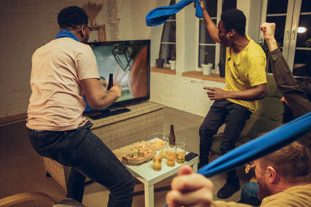 Group of friends watching TV, sport match together. Emotional fans cheering for favourite team,...