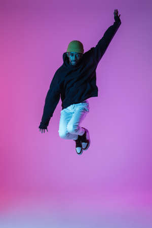Young stylish man in modern street style outfit isolated on gradient background in neon light. African-american fashionable model in look book, musician performing.の写真素材