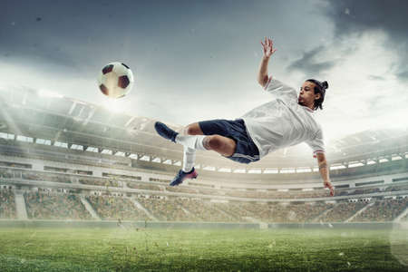 Male soccer, football player catching ball in jump at the stadium during sport match on dark sky backgroundの写真素材