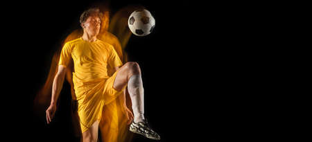 Young caucasian male football or soccer player kicking ball for the goal in mixed light on dark background. Concept of healthy lifestyle, professional sport, hobby.の写真素材