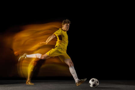 Young caucasian male football or soccer player kicking ball for the goal in mixed light on dark background. Concept of healthy lifestyle, professional sport, hobby.の写真素材