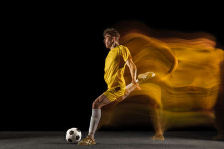 Young caucasian male football or soccer player kicking ball for the goal in mixed light on dark background. Concept of healthy lifestyle, professional sport, hobby.の写真素材