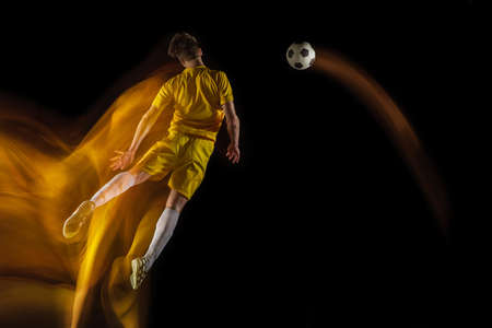 Young caucasian male football or soccer player kicking ball for the goal in mixed light on dark background. Concept of healthy lifestyle, professional sport, hobby.の写真素材