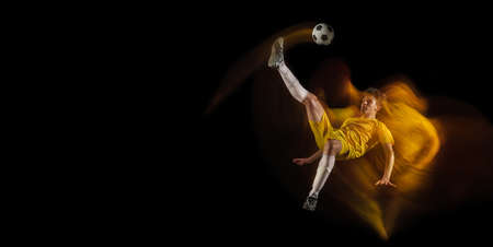 Young caucasian male football or soccer player kicking ball for the goal in mixed light on dark background. Concept of healthy lifestyle, professional sport, hobby.の写真素材