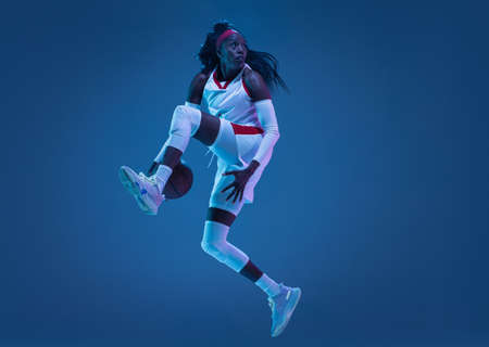 Beautiful african-american female basketball player in motion and action in neon light on blue...