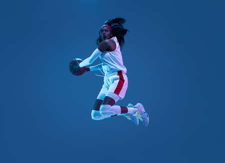 Beautiful african-american female basketball player in motion and action in neon light on blue...