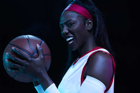 Beautiful african-american female basketball player in motion and action in neon light on black...