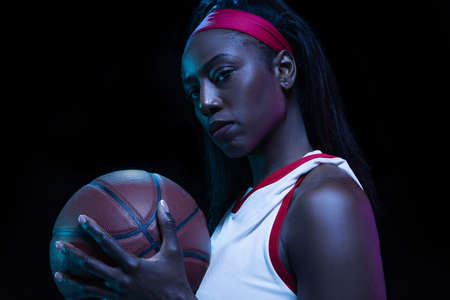 Beautiful african-american female basketball player in motion and action in neon light on black background. Concept of healthy lifestyle, professional sport, hobby.の写真素材