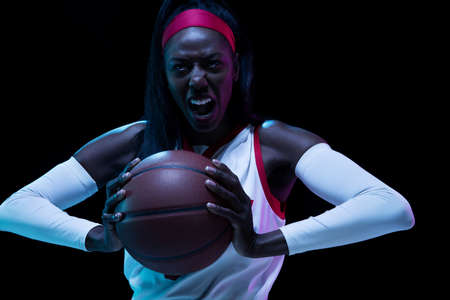 Beautiful african-american female basketball player in motion and action in neon light on black...