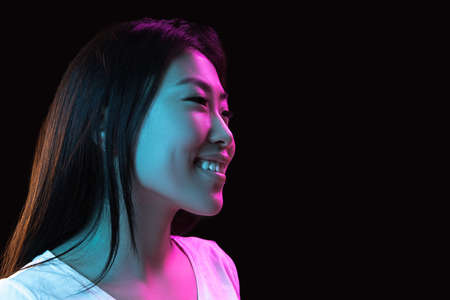 Asian young womans portrait on dark studio background in neon. Concept of human emotions, facial expression, youth, sales, ad.の写真素材