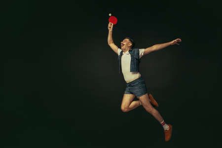 Young caucasian man playing tennis isolated on black studio background in retro style, action and motion conceptの写真素材