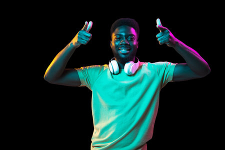 African young mans portrait on dark studio background in neon. Concept of human emotions, facial expression, youth, sales, ad.の写真素材
