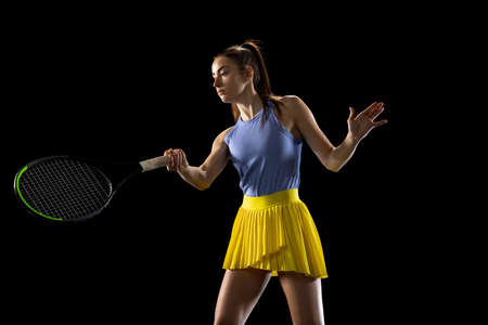 Young caucasian woman playing tennis isolated on black studio background in action and motion, sport conceptの写真素材