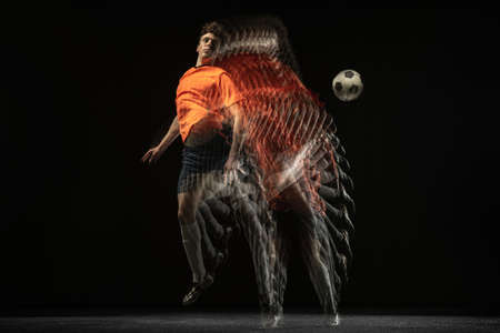 Young caucasian football soccer player in motion and action in mixed light on dark background.