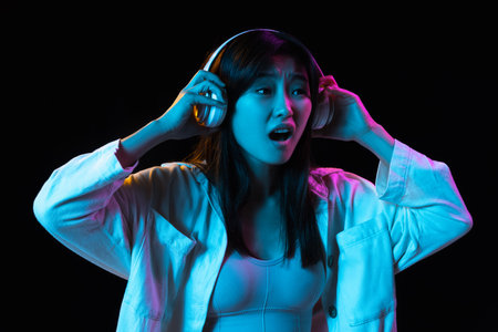 Asian young womans portrait on dark studio background in neon. Concept of human emotions, facial expression, youth, sales, ad.の写真素材