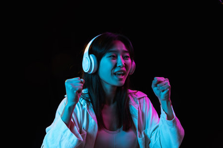 Asian young womans portrait on dark studio background in neon. Concept of human emotions, facial...