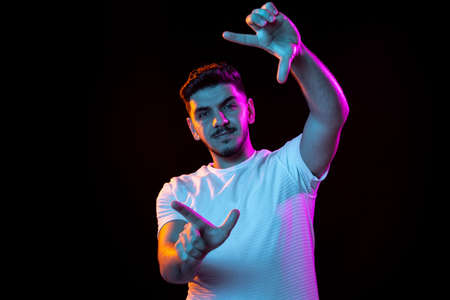 Young mans portrait on black studio background in neon light. Concept of human emotions, facial...