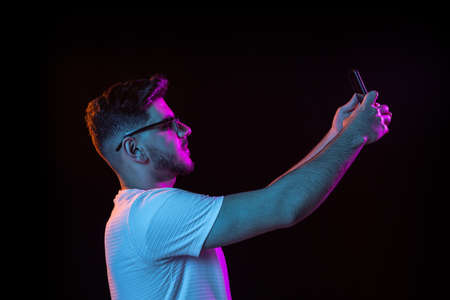 Young mans portrait on black studio background in neon light. Concept of human emotions, facial...
