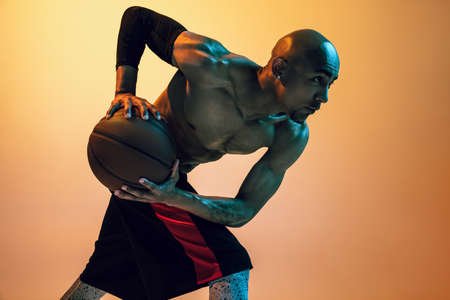 Close-up portrait of african-american male basketball player posing in neon light on orange...