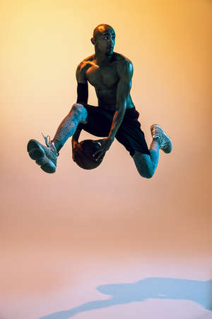 Portrait of african-american professional male basketball player in action in neon light on orange...
