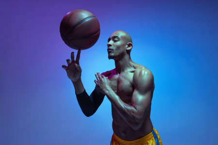 Strong muscular african-american male basketball player training in neon light on orange background.の写真素材
