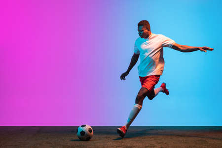 One African man, professional soccer football player training isolated on gradient blue pink background in neon light.の写真素材