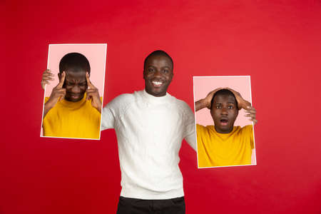 Young african man holding his portraits isolated over red studio background with copyspace for ad.
