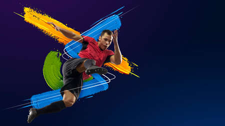 Young man, soccer footbal player training isolated in neon light on blue background. Art collage. Watercolor paints. Concept of sport, game, action.の写真素材