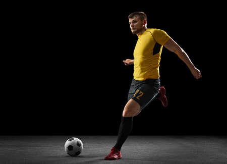 Powerful, flying above the field. Young football, soccer player in action, motion isolated on black studio background .の写真素材