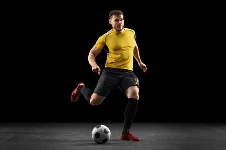 Powerful, flying above the field. Young football, soccer player in action, motion isolated on black studio background .の写真素材