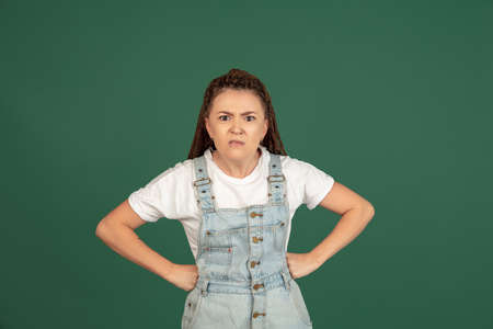 Beautiful female portrait isolated on green studio backgroud. The young emotional angry woman is...