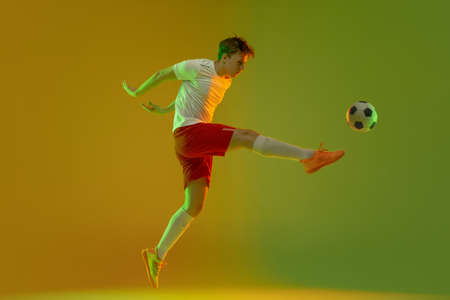One male soccer football player in action and motion isolated on gradient green yellow background in neon lightの写真素材
