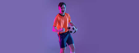 Half-length portrait of professional football player standing isolated on gradient blue pink background in neon light. Concept of sport, beauty.の写真素材