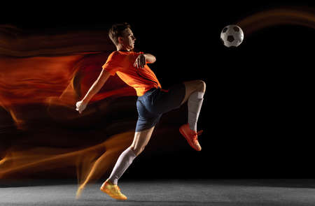 Young caucasian male football or soccer player kicking ball for the goal in mixed light on dark background. Concept of healthy lifestyle, professional sport, hobby.の写真素材