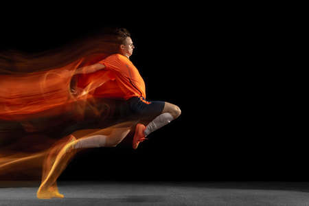 Young caucasian male football or soccer player kicking ball for the goal in mixed light on dark...