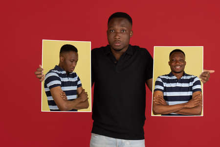 Young african man holding his portraits isolated over red studio background with copyspace for ad.の写真素材