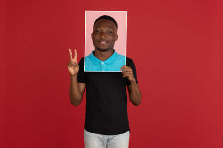 Young african man holding his portrait isolated over red studio background with copyspace for ad.の写真素材