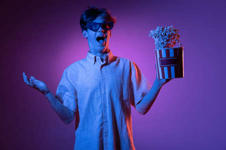 Excited in 3D eyewear and with popcorn. Caucasian mans portrait isolated on blue studio background...