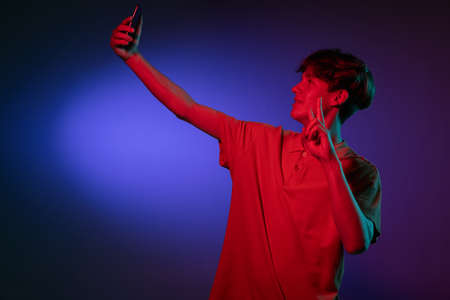 Caucasian young man with phone isolated on blue studio background in neon. Concept of human...
