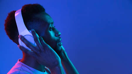 African-american young mans portrait on dark studio background in neon. Concept of human emotions, facial expression, youth, sales, ad.の写真素材