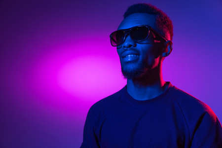 African-american young mans portrait on dark studio background in neon. Concept of human emotions,...