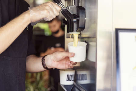 Human hand holding cone with twisted ice cream from machineの写真素材