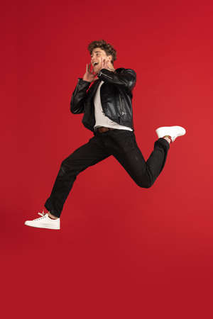 Jumping high, stylish. Young male portrait isolated on red studio background with copyspace for ad.の写真素材
