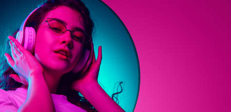 Young beautiful Caucasian girl listening to music isolated over multicolors background in neon light. Concept of beauty, fashion,ad. Flyerの写真素材