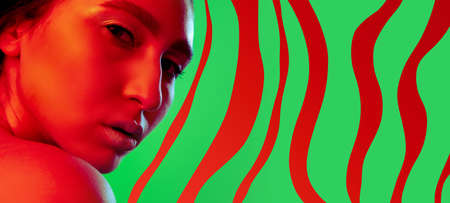 Close-up young beautiful Asian girl isolated over green red striped background in neon light. Concept of beauty, fashion,ad. Flyerの写真素材