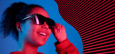 Young beautiful African girl in black sun glasses isolated over blue striped background in neon light. Concept of beauty, fashion,ad. Flyerの写真素材