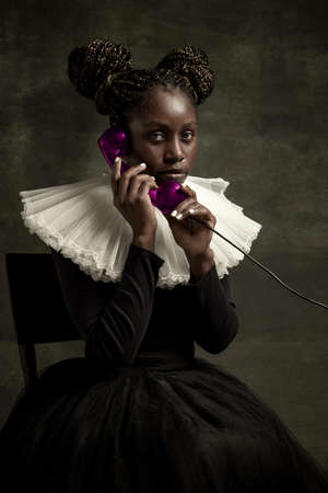 Portrait of medieval African young woman in black vintage dress with big white collar posing isolated on dark green background.の写真素材